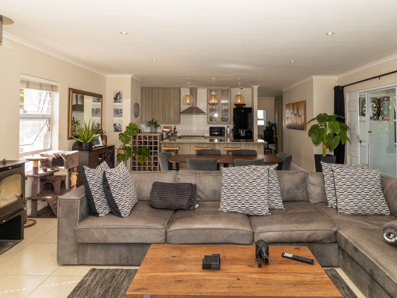 Spacious open-plan living area featuring a modern kitchen with island, tiled floors, and a prominent freestanding wood-burning fireplace, flowing out to the patio.