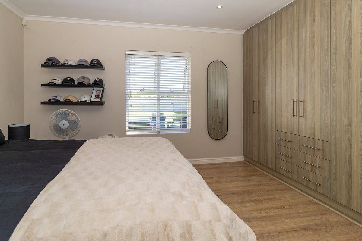 A well-maintained bedroom featuring extensive built-in wooden cabinetry, laminate flooring, and natural light through a window with fitted venetian blinds.