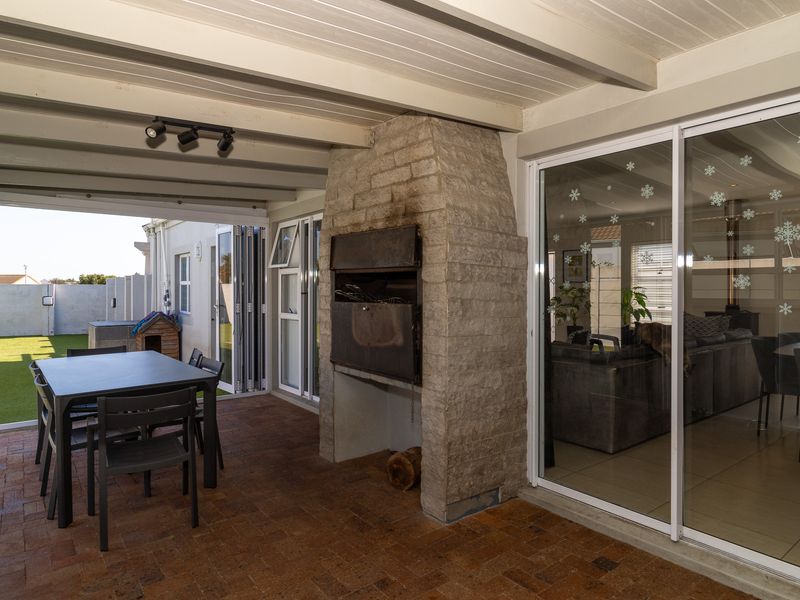 Covered patio featuring a built-in brick braai, brick paving, and sliding glass doors providing seamless access to the interior living area and garden.