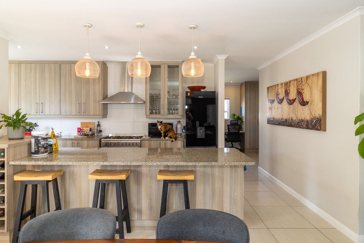 Modern kitchen featuring granite countertops, light wood cabinetry, a gas stove with extractor fan, and a built-in wine rack, finished with tiled flooring.