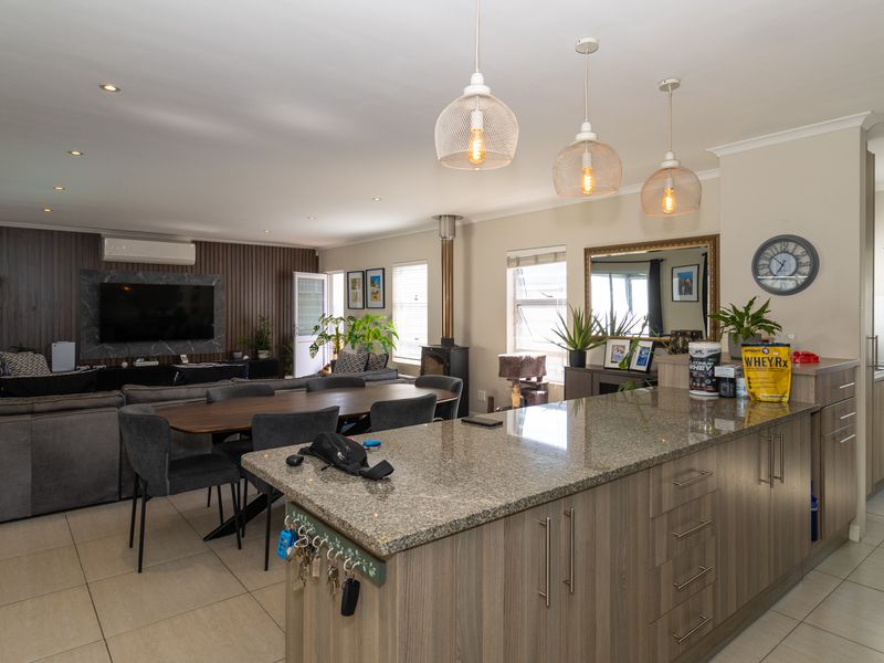 Spacious open-plan living and kitchen area featuring a granite island, wood-burning fireplace, modern pendant lighting, and a stylish timber slat feature wall.