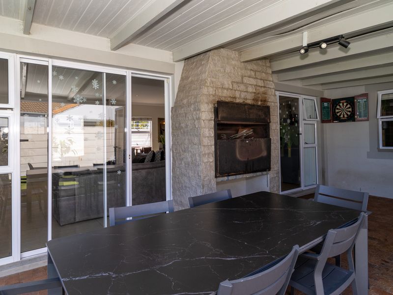 Covered patio area featuring a built-in stone braai, exposed beam ceiling, and direct access to the interior through sliding glass doors.