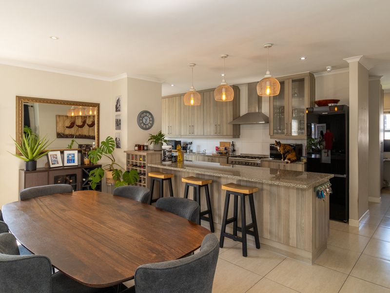 Spacious open-plan kitchen and dining area featuring modern wood-finish cabinetry, granite countertops, a breakfast bar, and tiled flooring throughout.