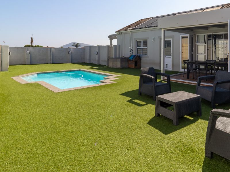 A well-maintained outdoor area featuring a swimming pool, artificial lawn, and a covered patio with bi-fold doors providing seamless indoor-outdoor flow.