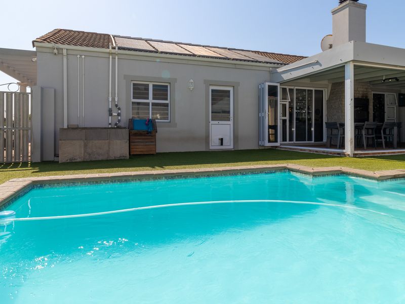 A well-maintained outdoor area featuring a swimming pool, artificial lawn, and a covered patio with bi-fold doors leading into the home.