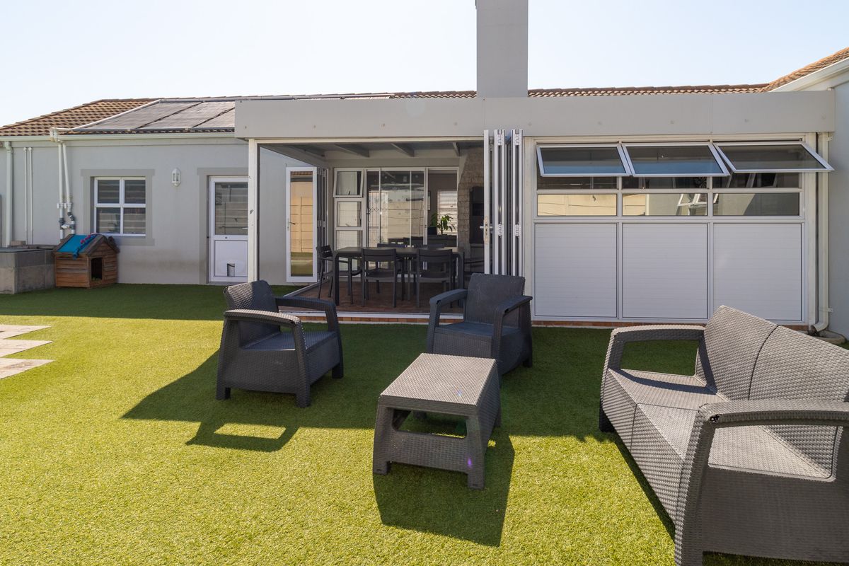 Rear exterior view featuring a covered patio with bi-fold doors, artificial lawn, and a swimming pool, ideal for outdoor entertaining.
