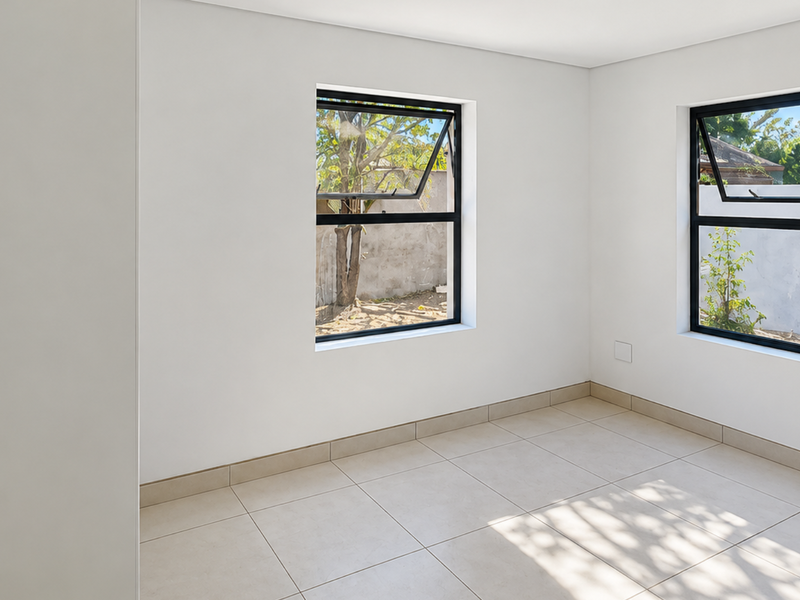 A bright, empty bedroom featuring neutral tiled flooring and modern black aluminium windows, offering a clean and versatile space ready for personalization.