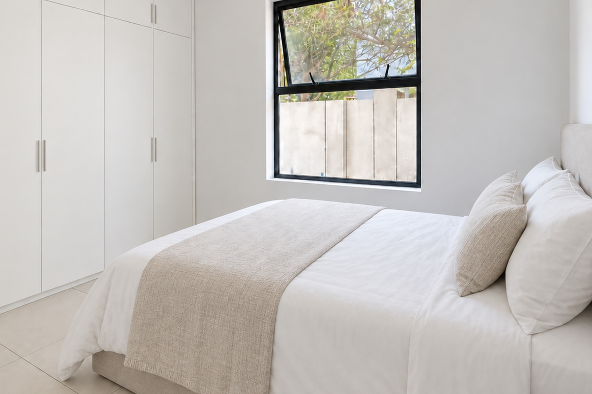 A bright and modern bedroom featuring neutral tones, built-in floor-to-ceiling cupboards, and large aluminium-framed windows providing natural light.