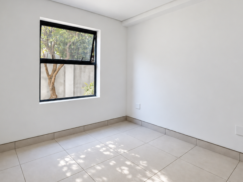 A bright, empty bedroom featuring neutral tiled flooring, built-in shelving, and a modern black-framed window overlooking the exterior.