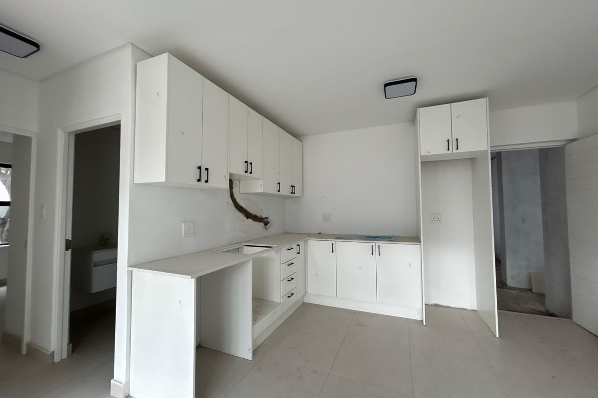 An unfinished kitchen space featuring white built-in cabinetry, tiled flooring, and prepared utility connections, awaiting final appliance installation and finishing touches.