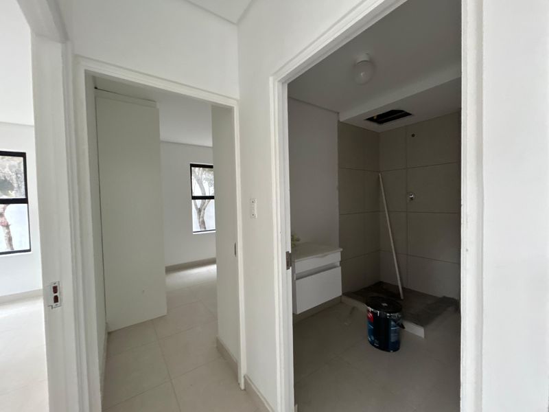 A view from the hallway looking into an unfinished bathroom with tiled shower area and vanity, adjacent to an empty bedroom space.