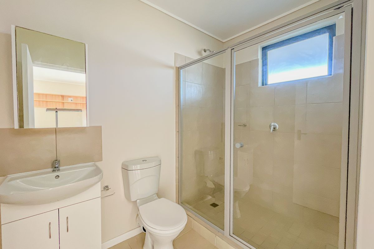 A clean and functional bathroom featuring a vanity with basin, a toilet, and a glass-enclosed shower with tiled walls.