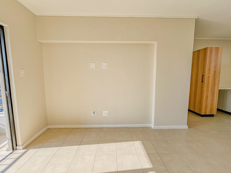 An empty living area featuring neutral tiled flooring, built-in storage cabinetry, and a sliding glass door leading to an outdoor space.
