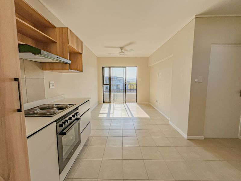 Open-plan kitchen and living area featuring tiled floors, built-in cabinetry, integrated oven and hob, and access to a balcony through sliding glass doors.