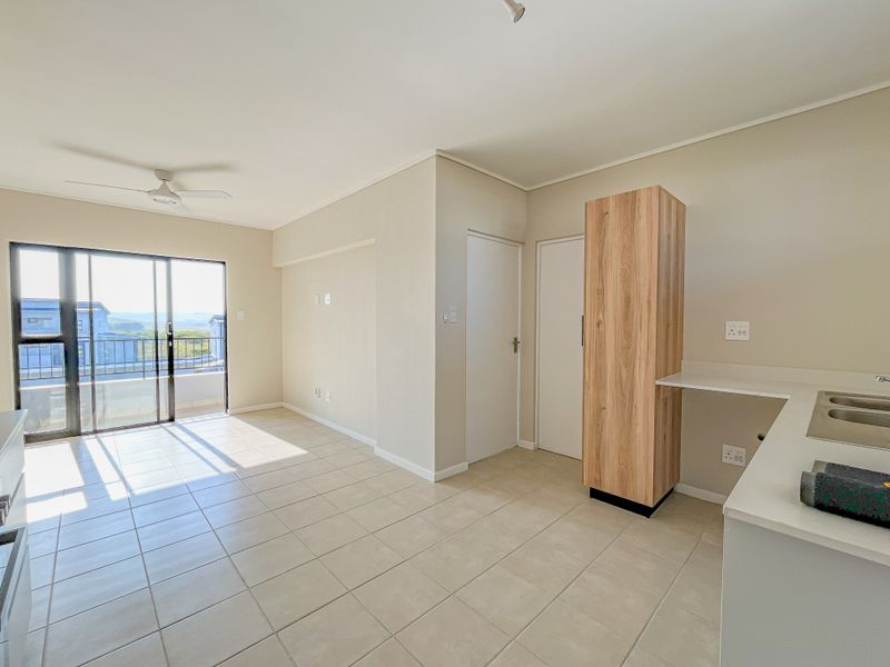 An open-plan living and kitchen area featuring neutral tiled flooring, built-in cabinetry, and a sliding glass door leading to a balcony.
