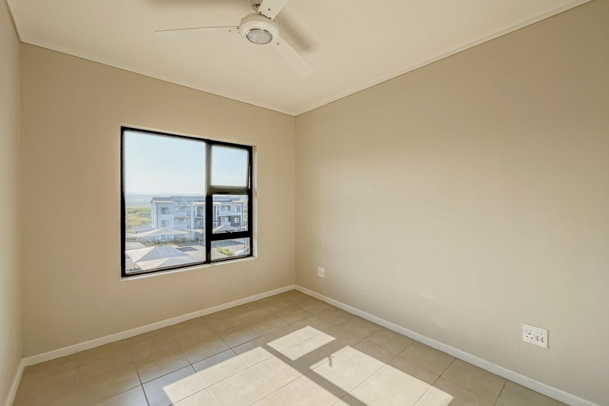 A bright, empty bedroom featuring neutral wall paint, tiled flooring, and a ceiling fan, with a window offering an exterior view.
