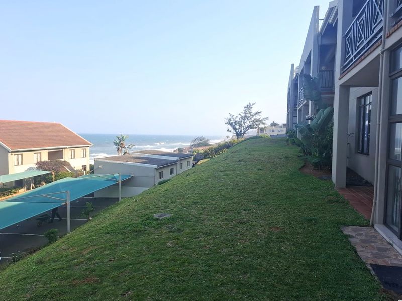 A view of the rear exterior of the apartment complex featuring a grassy slope, balconies, and a view of the ocean.