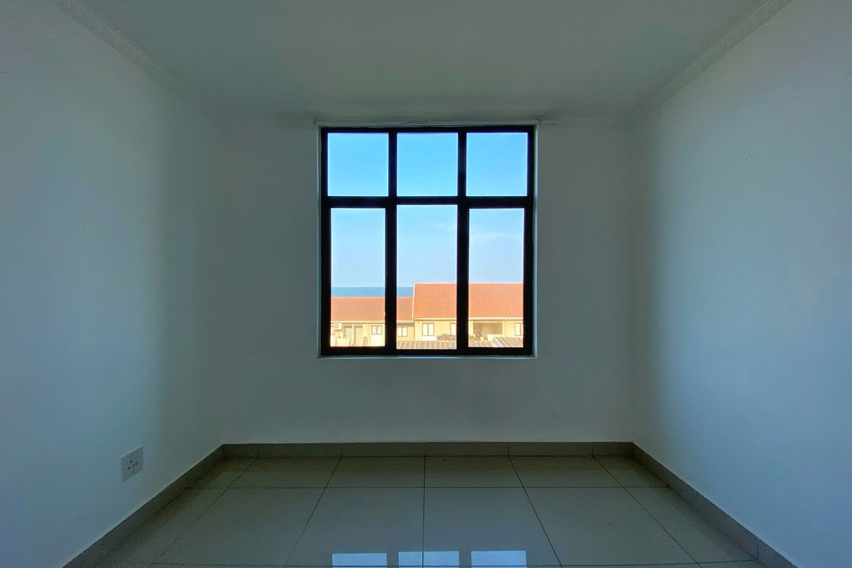 A bright, empty bedroom featuring neutral tiled flooring, clean white walls, and a large window with a view of the surrounding neighborhood.