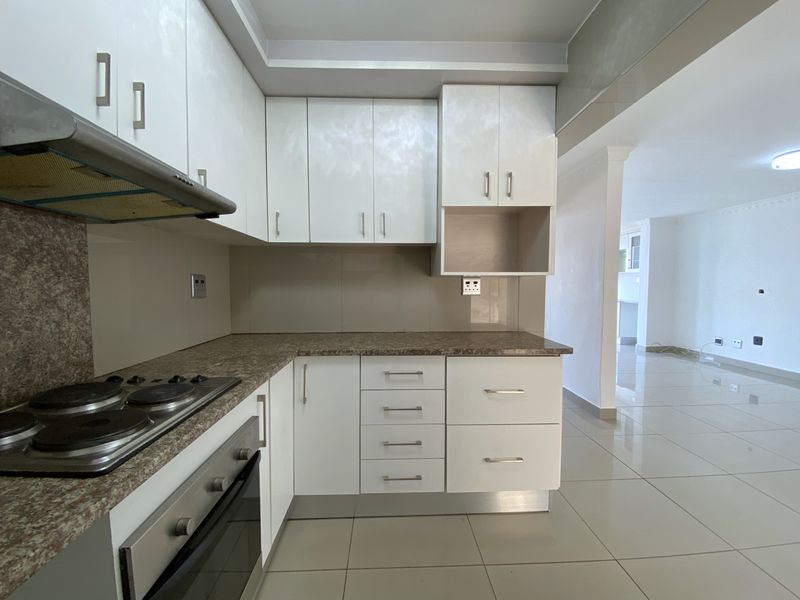 A clean, modern kitchen featuring white built-in cabinetry, a laminate countertop, an integrated electric hob, and an oven, with neutral tiled flooring throughout.