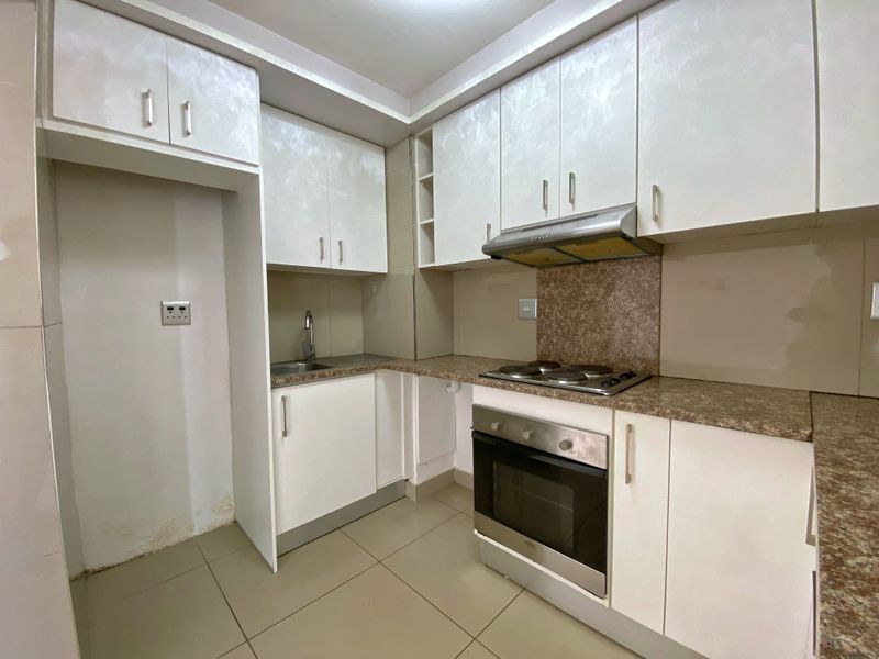 A compact kitchen featuring white built-in cabinetry, laminate countertops, a built-in oven, and an electric hob with an extractor fan.