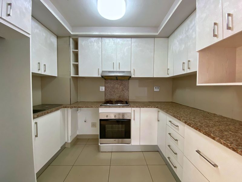A clean, functional kitchen featuring white cabinetry, laminate countertops, a built-in oven, and an electric hob with an extractor fan.