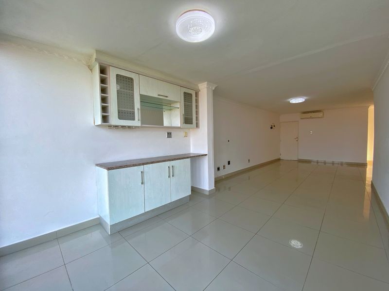 Spacious open-plan living area featuring tiled flooring, built-in cabinetry, and a wall-mounted air conditioning unit in a neutral, well-lit setting.