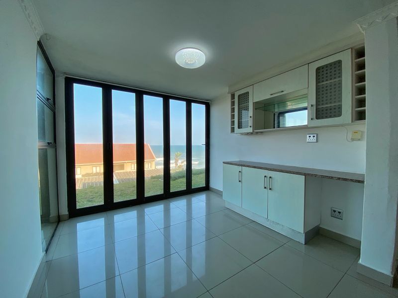 An empty living area featuring tiled floors, built-in cabinetry, and large glass doors offering scenic ocean views.