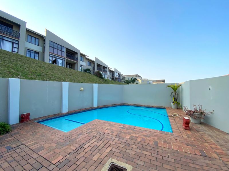 Private swimming pool area featuring brick paving and a surrounding boundary wall, set against the backdrop of the apartment complex.