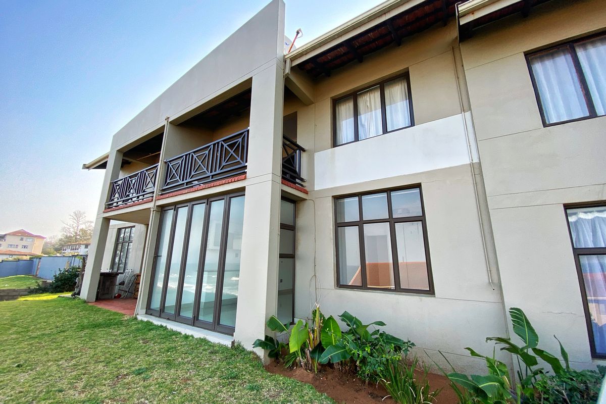 Rear view of the apartment building featuring a ground floor patio with sliding glass doors and an upper level balcony with dark metal railings.