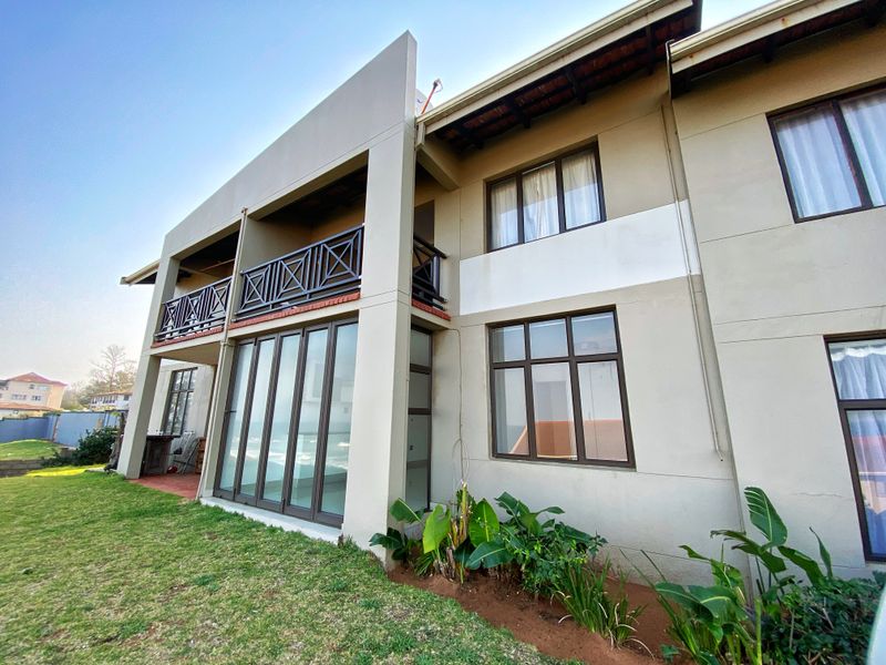 Rear view of the apartment building featuring a ground floor patio with sliding glass doors and an upper level balcony with dark metal railings.