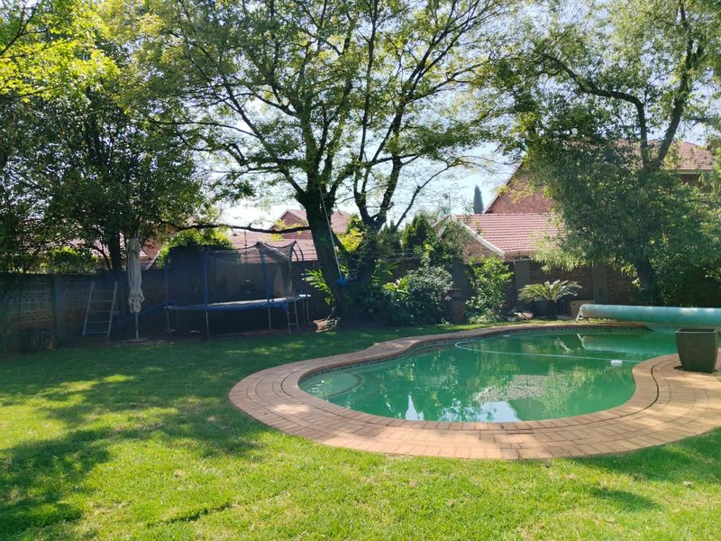 A private backyard featuring a swimming pool with brick coping, surrounded by a lush lawn and mature trees.