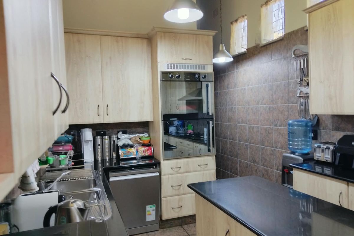 A functional kitchen featuring light wood cabinetry, dark granite countertops, a double eye-level oven, and tiled wall finishes.