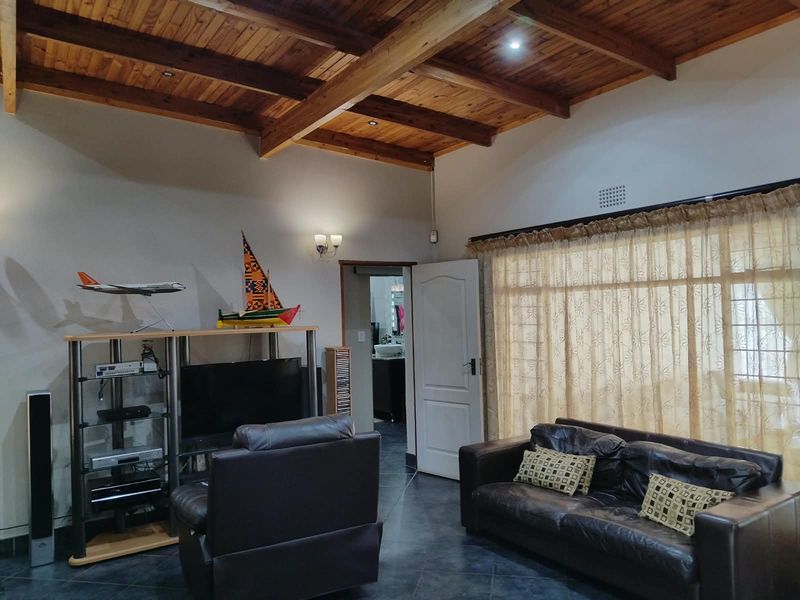 A living room featuring a high exposed timber beam ceiling, tiled flooring, and direct access to an adjacent room.