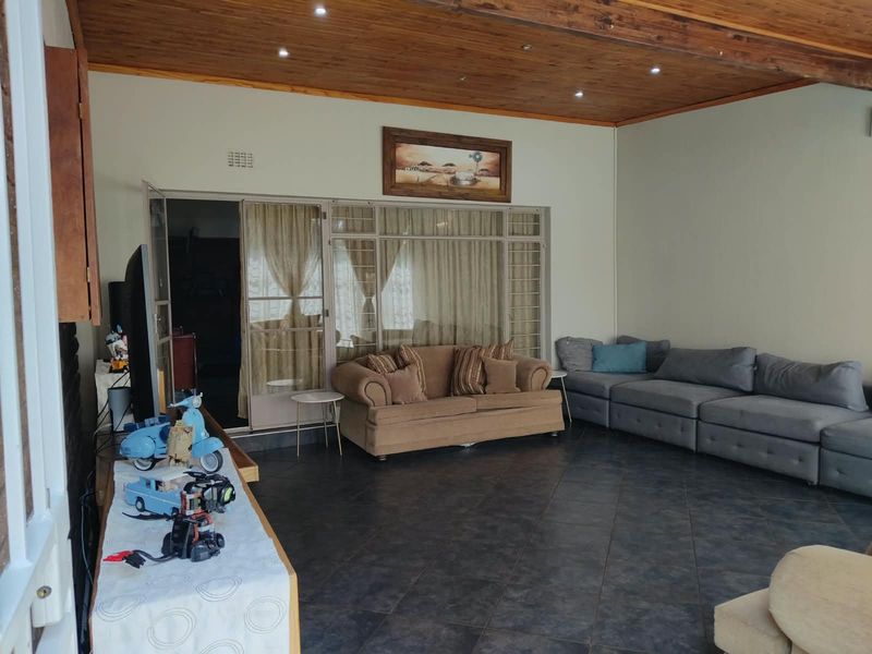 Spacious living room featuring dark tiled flooring, a warm timber-paneled ceiling with recessed lighting, and large sliding glass doors leading to an adjacent area.