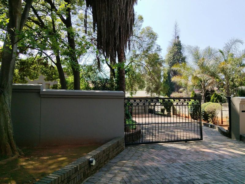 Front entrance view featuring a secure metal driveway gate, paved driveway, and perimeter walling surrounded by established trees and landscaping.