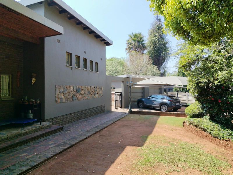 Rear exterior view featuring a modern grey facade with stone cladding, a paved walkway, and a covered carport area.