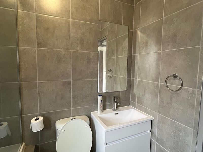Modern bathroom featuring full-height grey tiling, a wall-mounted vanity with basin, toilet, and a glass shower screen.