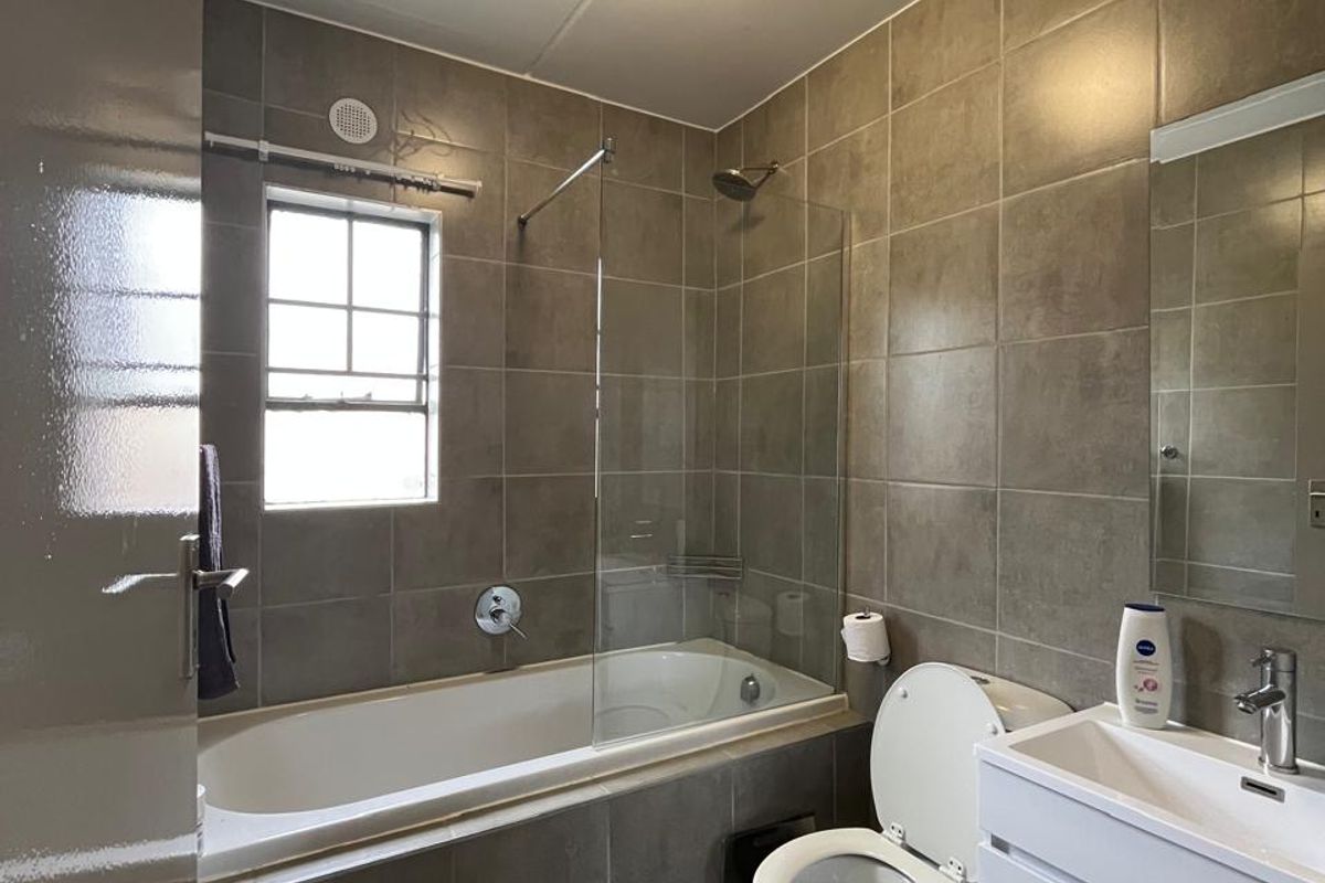 A modern bathroom featuring a bathtub with a glass shower screen, a wall-mounted vanity with a basin, and neutral floor-to-ceiling wall tiles.