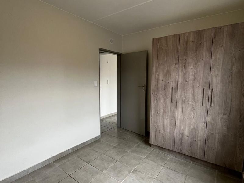 A clean, empty bedroom featuring neutral tiled flooring, a built-in wooden wardrobe, and a simple ceiling light fixture.