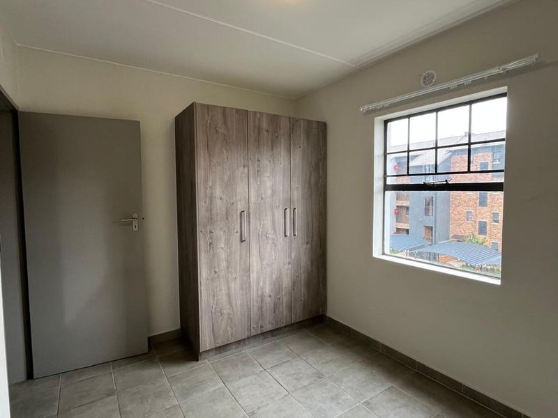 A clean, empty bedroom featuring neutral tiled flooring, a built-in wooden wardrobe, and a window providing natural light.