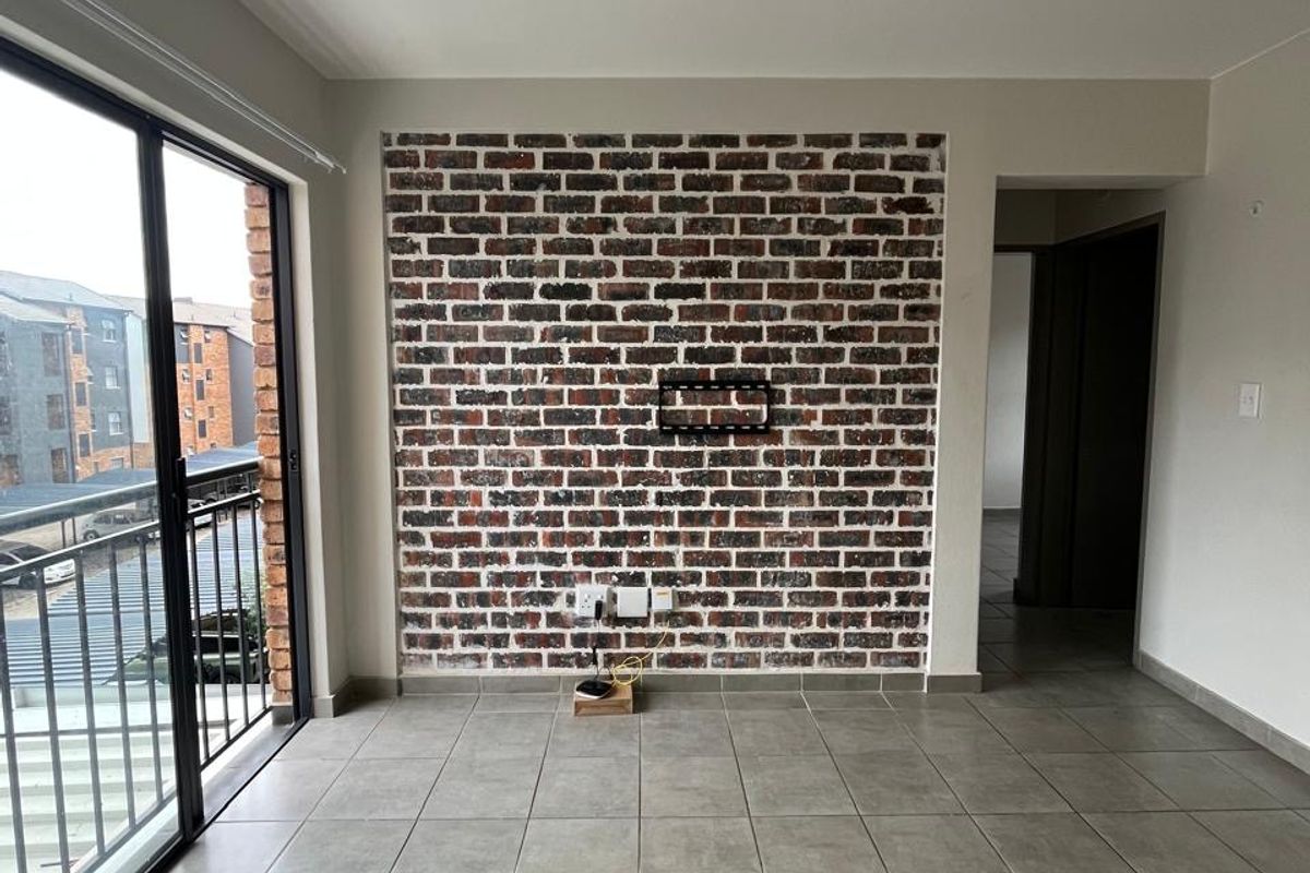 Bright living area featuring a stylish exposed brick accent wall, neutral floor tiles, and direct access to a private balcony through sliding glass doors.