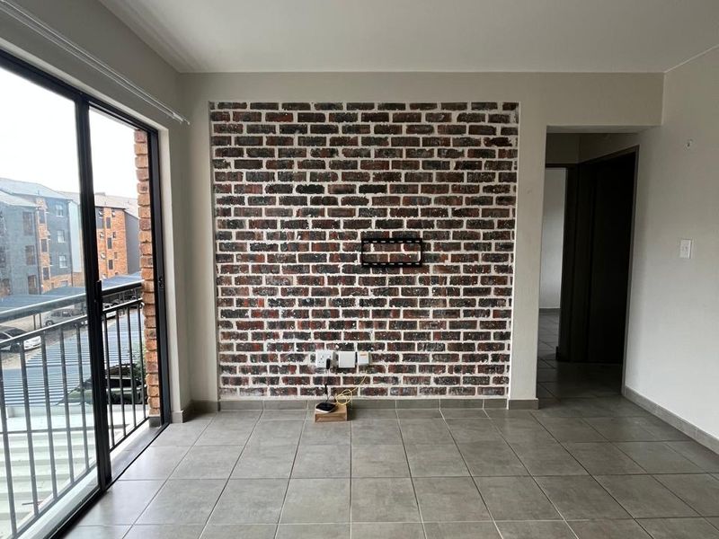 Bright living area featuring a stylish exposed brick accent wall, neutral floor tiles, and direct access to a private balcony through sliding glass doors.