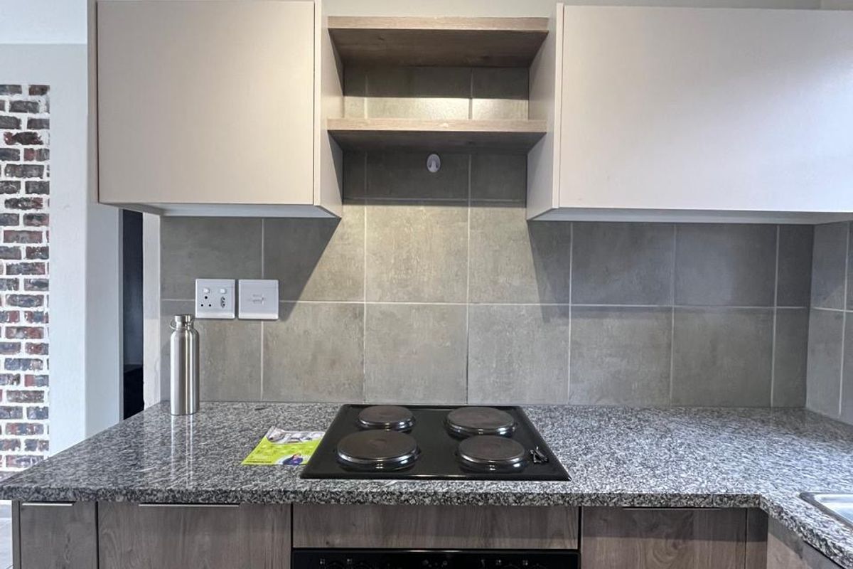 A modern kitchen featuring granite countertops, a built-in electric oven and hob, and neutral-toned cabinetry with a tiled backsplash.