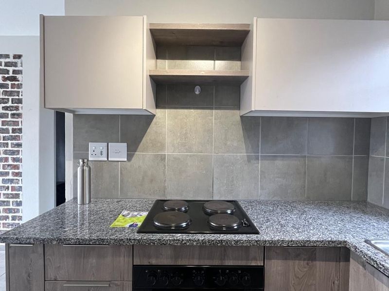 A modern kitchen featuring granite countertops, a built-in electric oven and hob, and neutral-toned cabinetry with a tiled backsplash.