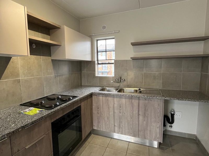 A clean, modern kitchen featuring wood-finish cabinetry, granite countertops, a built-in oven and hob, double sink, and neutral tiled flooring.