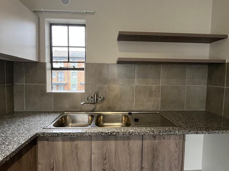 A clean and functional kitchen area featuring granite countertops, wood-look cabinetry, a double stainless steel sink, and open shelving with a tiled backsplash.