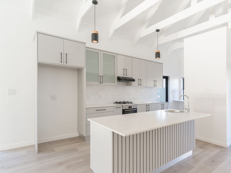 Modern kitchen featuring light grey cabinetry, stone countertops, a central island, gas hob, and vaulted ceilings with exposed rafters.