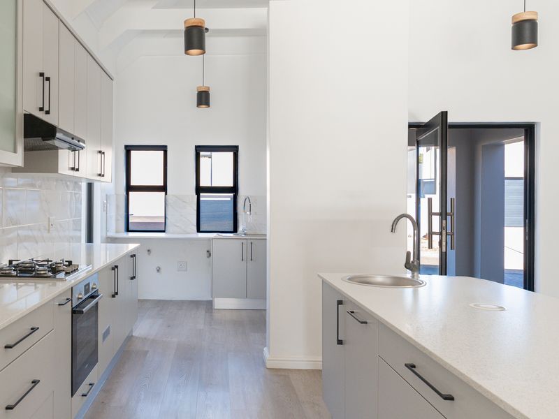 Modern kitchen featuring light grey cabinetry, stone countertops, a central island with sink, built-in gas hob, oven, and high-quality finishes throughout.