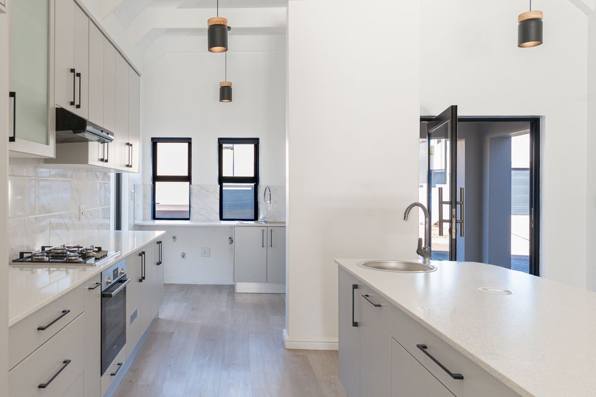 Modern kitchen featuring light grey cabinetry, stone countertops, a central island with sink, built-in gas hob, oven, and high-quality finishes throughout.