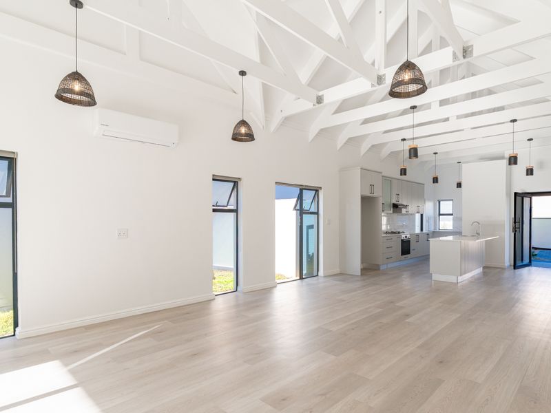 Spacious open-plan living and kitchen area featuring high vaulted ceilings with exposed trusses, modern cabinetry, and light laminate flooring.